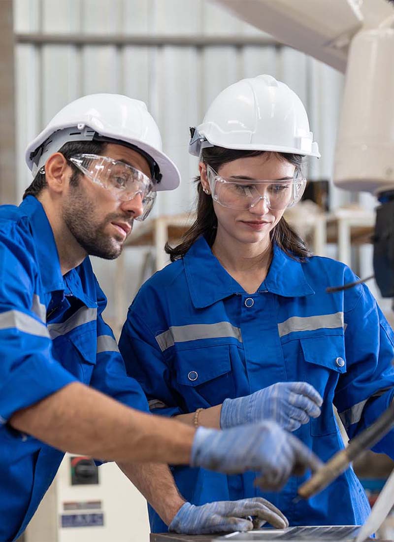 Male and female engineer using laptop working with robot arm welding machine in industrial factory. Team of technician automation robot in uniform explains robot arm system.